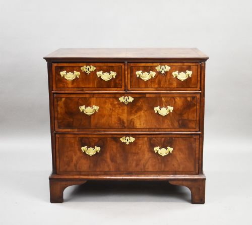 fig 1. A Georgian burr walnut chest of drawers featuring two short over two long drawers with brass drop handles and pierced escutcheons, supported by bracket feet.