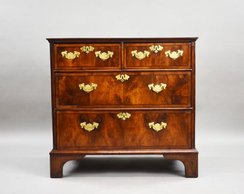 fig 2. A Georgian burr walnut chest of drawers featuring two short over two long drawers with brass drop handles and pierced escutcheons, supported by bracket feet.