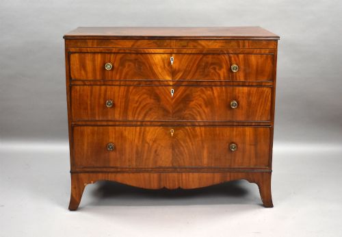 fig 1. A Regency mahogany chest of drawers featuring three full-length drawers with brass knobs, bone keyhole escutcheons, flame veneer fronts, and a shaped apron base.