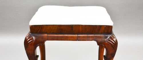 fig 2. A square Queen Anne style walnut stool featuring cream textured fabric upholstery and carved cabriole legs with shell motifs.