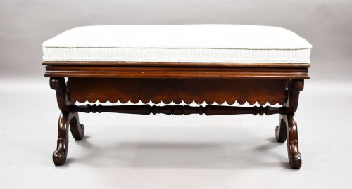fig 1. A William IV mahogany stool featuring a scalloped apron, carved scroll end supports, a turned central stretcher, and an off-white upholstered seat cushion.