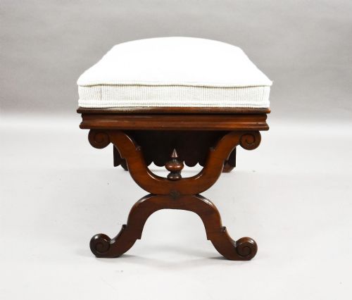 fig 2. A William IV mahogany stool featuring a scalloped apron, carved scroll end supports, a turned central stretcher, and an off-white upholstered seat cushion.