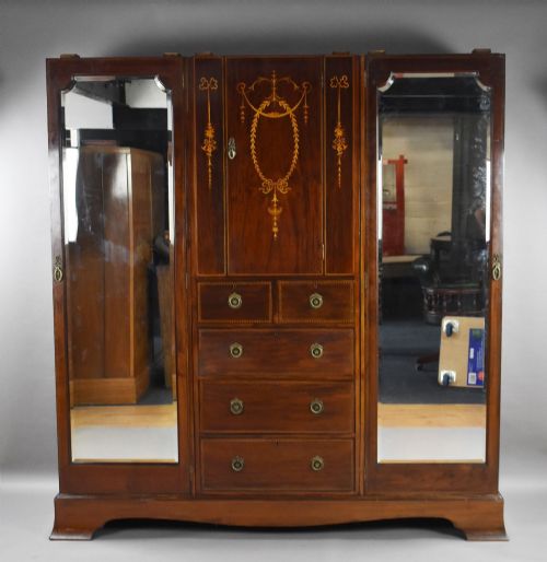 fig 3. An Edwardian mahogany triple wardrobe featuring twin full-length mirror doors flanking a central inlaid cupboard and four drawers.
