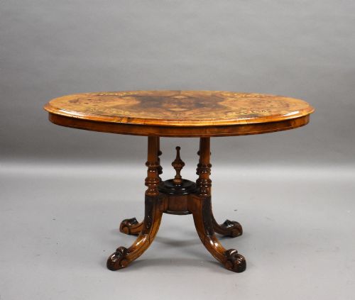 fig 1. An oval Victorian burr walnut coffee table with floral marquetry inlay, four turned columns, and carved splayed feet.