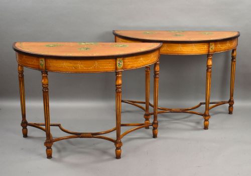 fig 1. A pair of Sheraton Revival demi-lune console tables in golden satinwood with hand-painted floral garlands, fluted tapered legs, and decorative stretchers.
