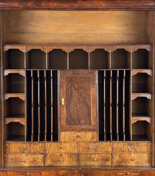 fig 3. A George II burr walnut bureau bookcase featuring an upper double-door cabinet with shaped mirrored panels over a fall-front desk and four drawers with brass handles.