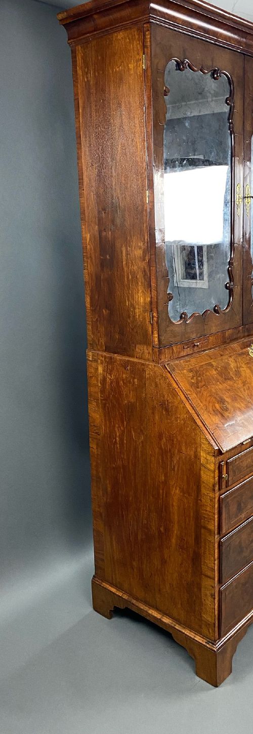 A George II burr walnut bureau bookcase featuring an upper double-door cabinet with shaped mirrored panels over a fall-front desk and four drawers with brass handles. View VIII