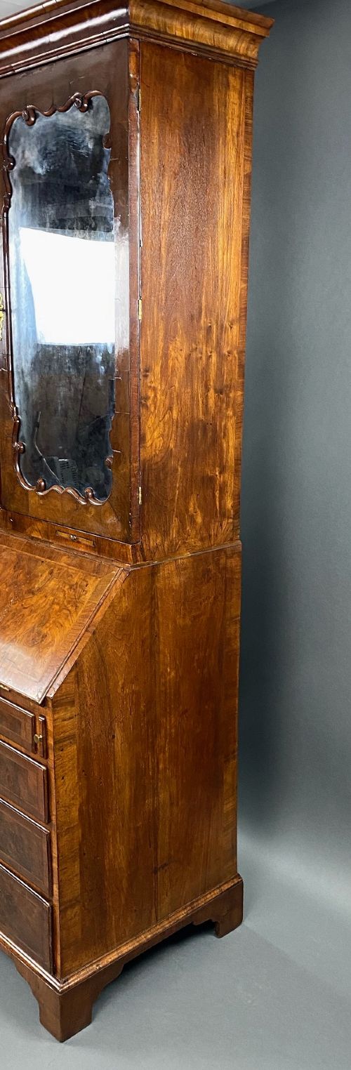 A George II burr walnut bureau bookcase featuring an upper double-door cabinet with shaped mirrored panels over a fall-front desk and four drawers with brass handles. View IX