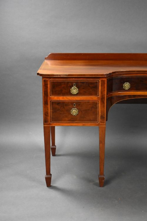 fig 1. A George III mahogany sideboard featuring an inlaid concave centre, multiple drawers with circular brass handles, and square tapered legs with spade feet.