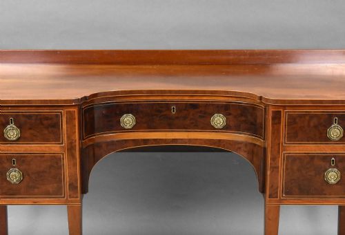 fig 2. A George III mahogany sideboard featuring an inlaid concave centre, multiple drawers with circular brass handles, and square tapered legs with spade feet.