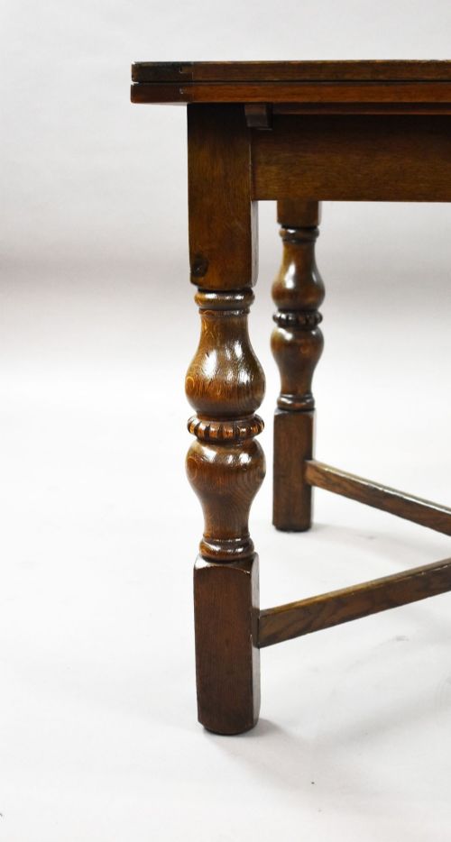 fig 4. An antique warm brown oak draw-leaf dining table surrounded by four matching carved wooden chairs with light upholstery.