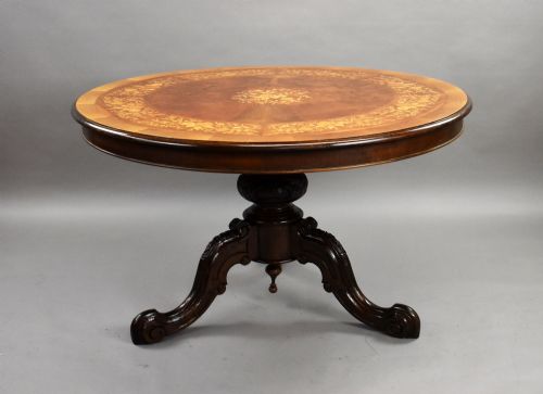 fig 1. A Victorian circular burr walnut centre table featuring floral marquetry inlays on the tabletop and a dark carved pedestal base.