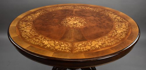 fig 3. A Victorian circular burr walnut centre table featuring floral marquetry inlays on the tabletop and a dark carved pedestal base.