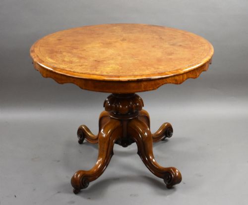 fig 2. An oval Victorian burr walnut loo table featuring geometric and floral marquetry inlay, shown upright via a tilt-top mechanism on a carved four-legged pedestal base.