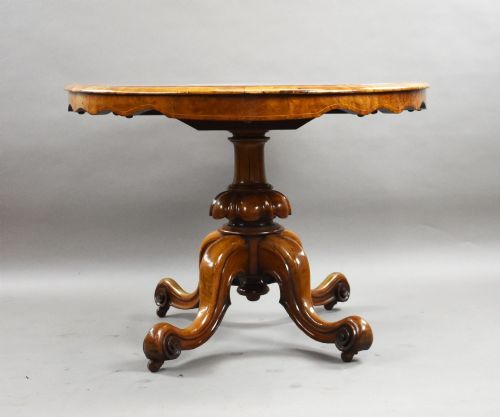 fig 3. An oval Victorian burr walnut loo table featuring geometric and floral marquetry inlay, shown upright via a tilt-top mechanism on a carved four-legged pedestal base.