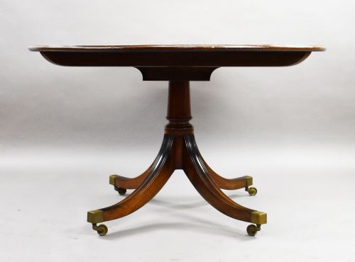 fig 2. An oval Regency style flame mahogany tilt-top dining table featuring a crossbanded satinwood border and a pedestal base with brass castors.