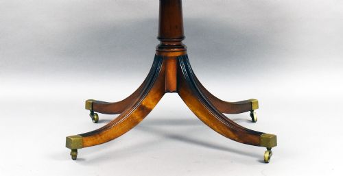 fig 4. An oval Regency style flame mahogany tilt-top dining table featuring a crossbanded satinwood border and a pedestal base with brass castors.