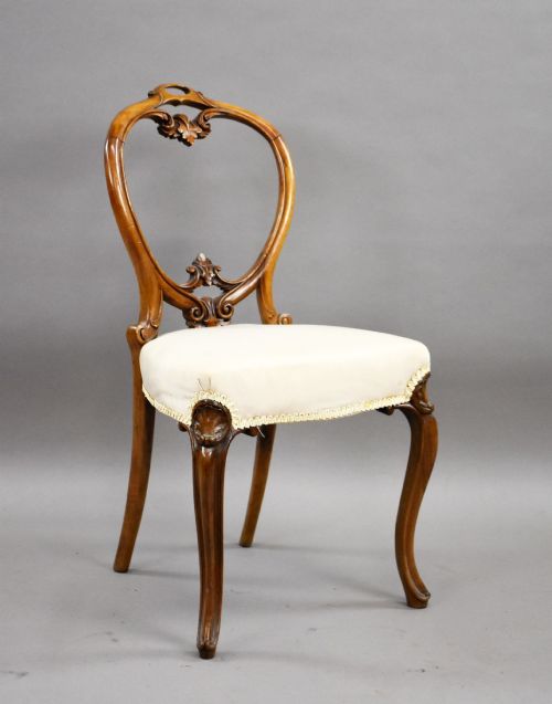fig 1. A set of four Victorian walnut balloon back dining chairs featuring carved back crests, cabriole front legs, and cream upholstered seats.