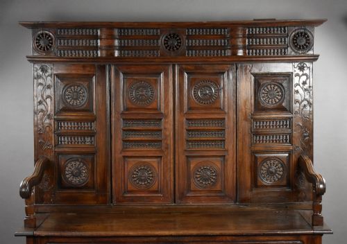 fig 2. A high-backed dark oak panelled settle featuring geometric roundel carvings, a spindle frieze, scroll arms, and a box seat storage base.