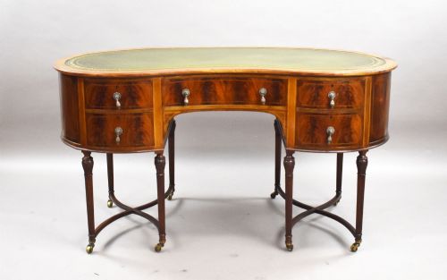 fig 1. An Edwardian kidney-shaped writing desk crafted from flame mahogany with a green leather writing surface, five drawers, turned fluted legs, and brass castors.