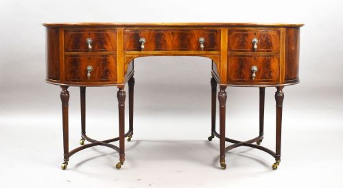 fig 2. An Edwardian kidney-shaped writing desk crafted from flame mahogany with a green leather writing surface, five drawers, turned fluted legs, and brass castors.
