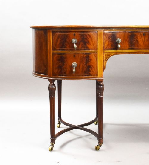 fig 3. An Edwardian kidney-shaped writing desk crafted from flame mahogany with a green leather writing surface, five drawers, turned fluted legs, and brass castors.