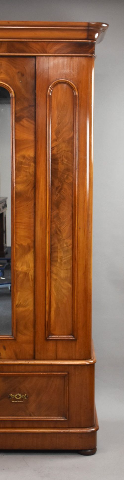 Victorian flame mahogany wardrobe featuring a central full-length arched mirror door flanked by arched wood panels, topped with a moulded cornice and resting on a base drawer. View IV