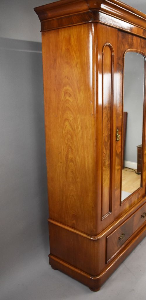 Victorian flame mahogany wardrobe featuring a central full-length arched mirror door flanked by arched wood panels, topped with a moulded cornice and resting on a base drawer. View VI