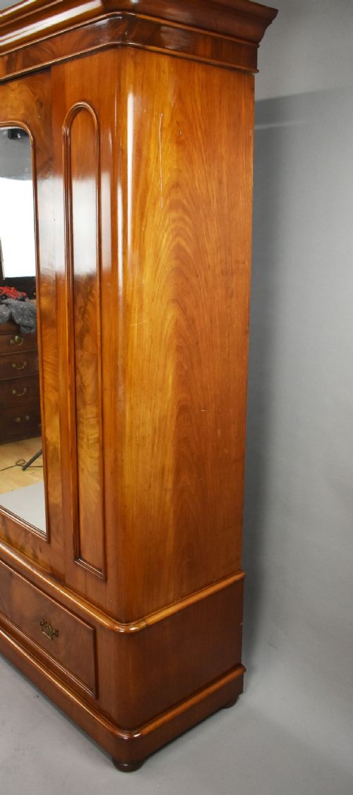 Victorian flame mahogany wardrobe featuring a central full-length arched mirror door flanked by arched wood panels, topped with a moulded cornice and resting on a base drawer. View VII