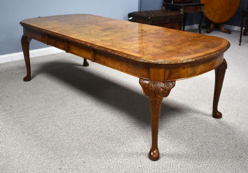 fig 1. A Queen Anne style burr walnut extending dining table shown with eight matching chairs featuring curved backrests and floral upholstered seats.
