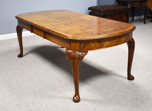 fig 2. A Queen Anne style burr walnut extending dining table shown with eight matching chairs featuring curved backrests and floral upholstered seats.