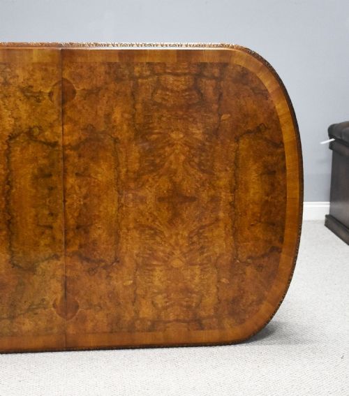 fig 5. A Queen Anne style burr walnut extending dining table shown with eight matching chairs featuring curved backrests and floral upholstered seats.