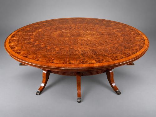 fig 1. A large oval burr walnut extending dining table with inlaid crossbanding and pedestal legs terminating in brass castors.