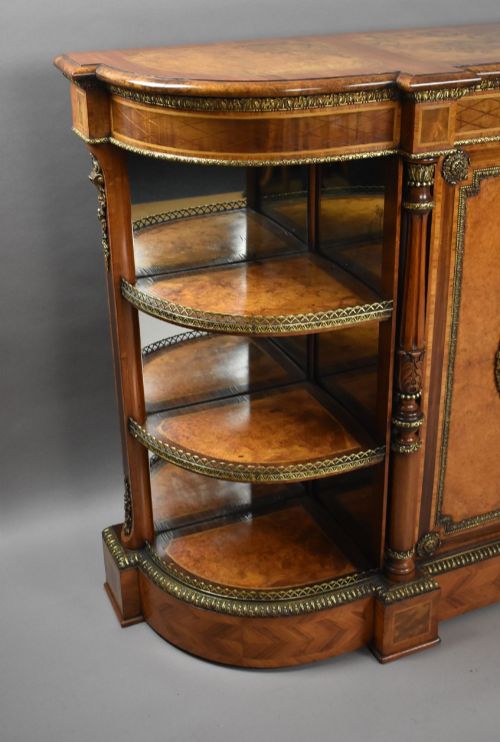 fig 1. A Victorian burr walnut credenza featuring central cupboard doors with oval porcelain plaques and gilt bronze mounts flanked by curved open display shelves.