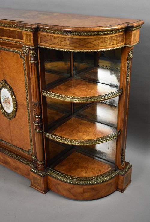 fig 4. A Victorian burr walnut credenza featuring central cupboard doors with oval porcelain plaques and gilt bronze mounts flanked by curved open display shelves.