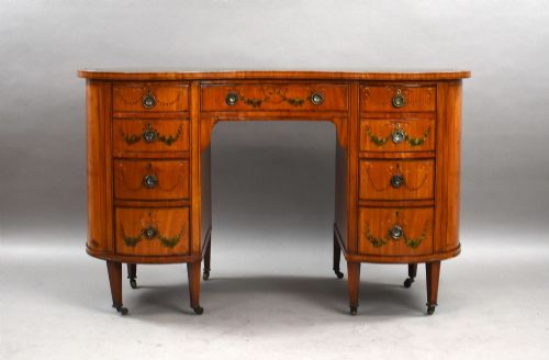 fig 1. An Edwardian satinwood kidney-shaped writing desk featuring nine hand-painted drawers with brass ring handles and tapered legs on castors.