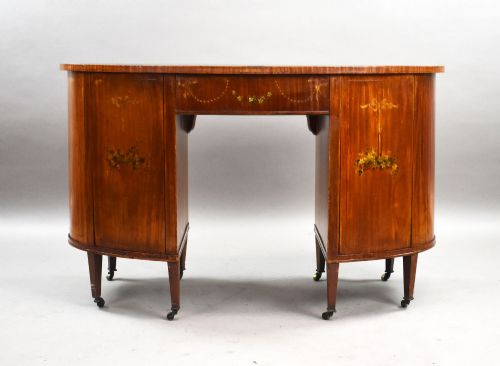 fig 3. An Edwardian satinwood kidney-shaped writing desk featuring nine hand-painted drawers with brass ring handles and tapered legs on castors.