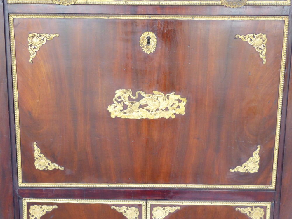 A dark mahogany drop-front escritoire cabinet featuring an open writing flap, fitted interior drawers, brass mounts, a black marble top, and carved paw feet. View V