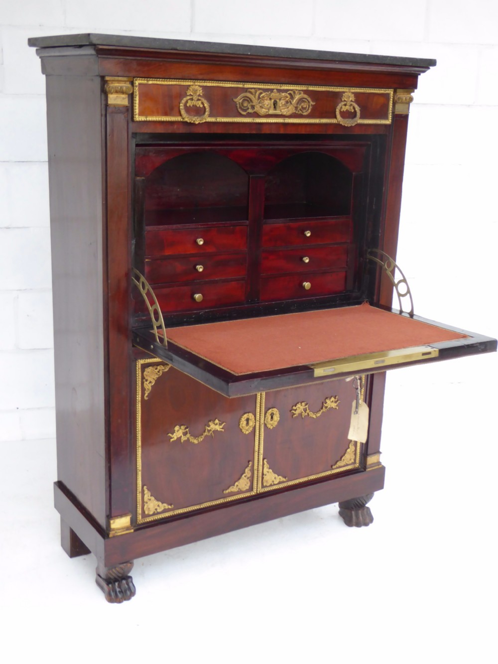 A dark mahogany drop-front escritoire cabinet featuring an open writing flap, fitted interior drawers, brass mounts, a black marble top, and carved paw feet. View VIII