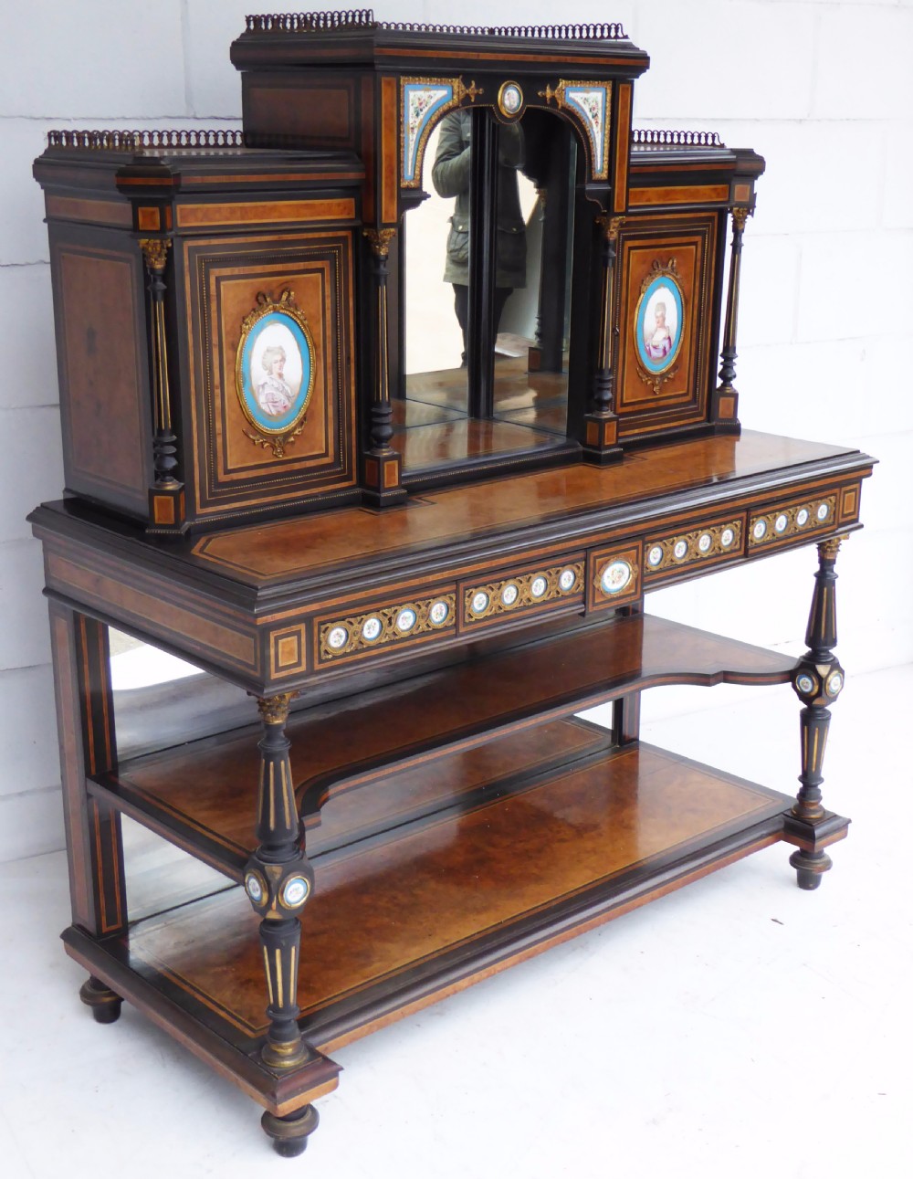 An ebonised and walnut 19th-century Bonheur du Jour writing desk featuring porcelain plaque inserts, gilded mounts, mirrors, and lower tier shelves.