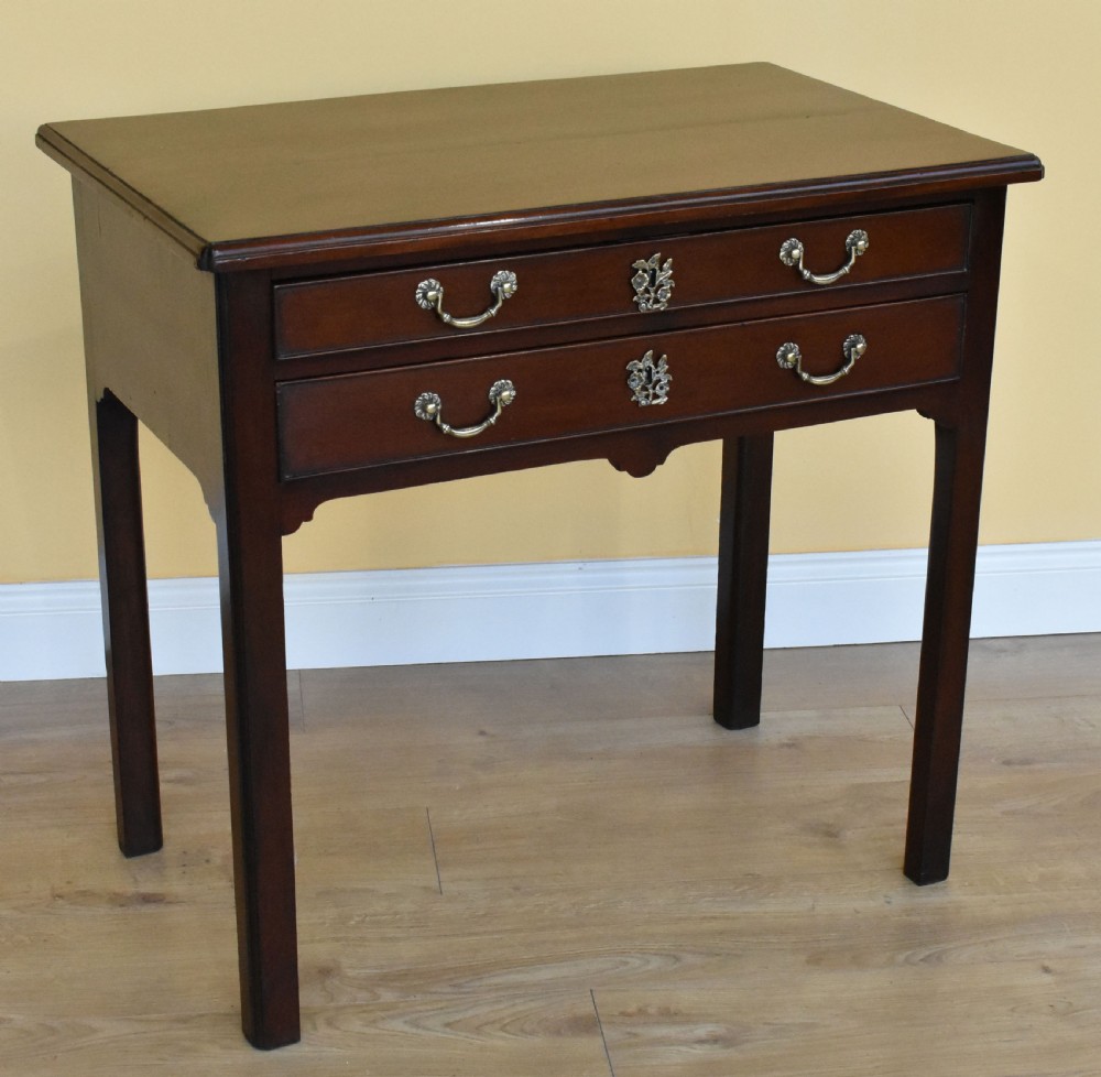 A George III mahogany side table featuring two drawers with brass swan-neck handles and decorative keyhole escutcheons, supported on straight square legs.