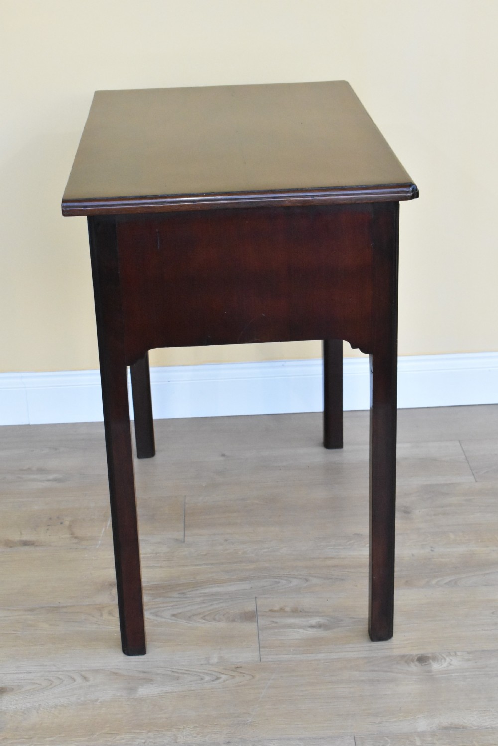 A George III mahogany side table featuring two drawers with brass swan-neck handles and decorative keyhole escutcheons, supported on straight square legs. View V
