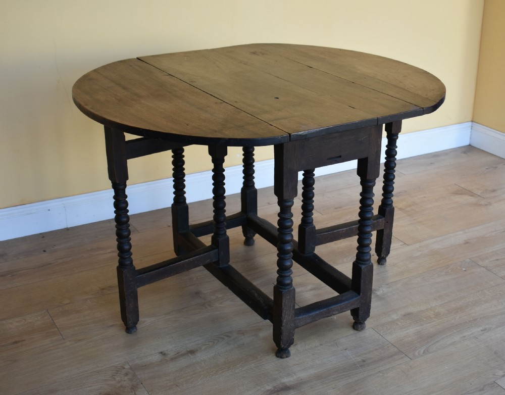 An eighteenth-century dark oak gateleg dining table with circular drop leaves and bobbin-turned legs standing on a wooden floor.