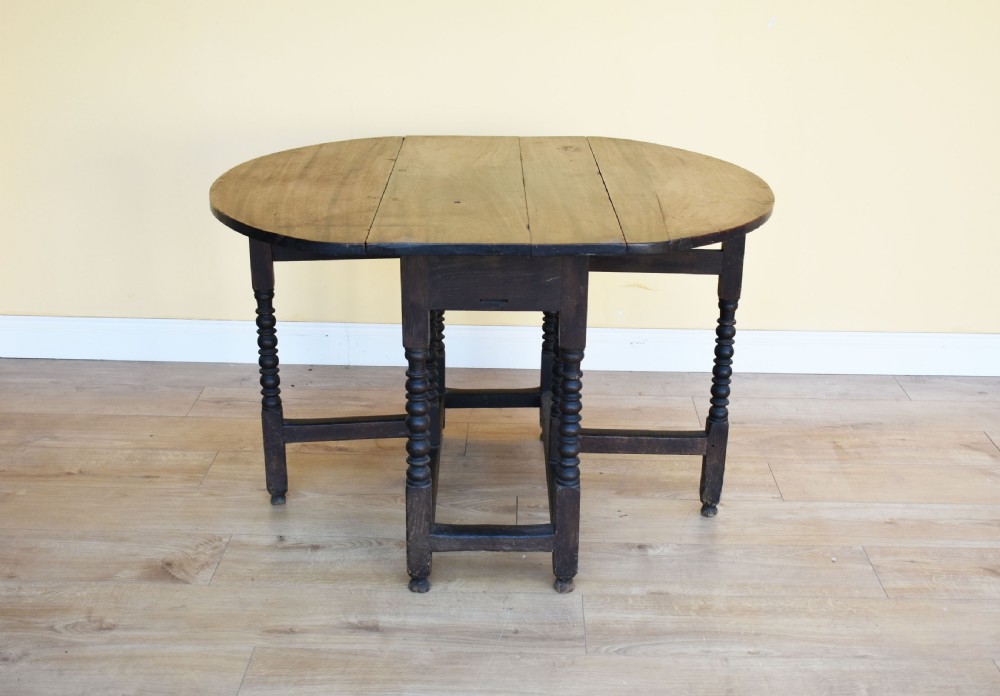 An eighteenth-century dark oak gateleg dining table with circular drop leaves and bobbin-turned legs standing on a wooden floor. View II