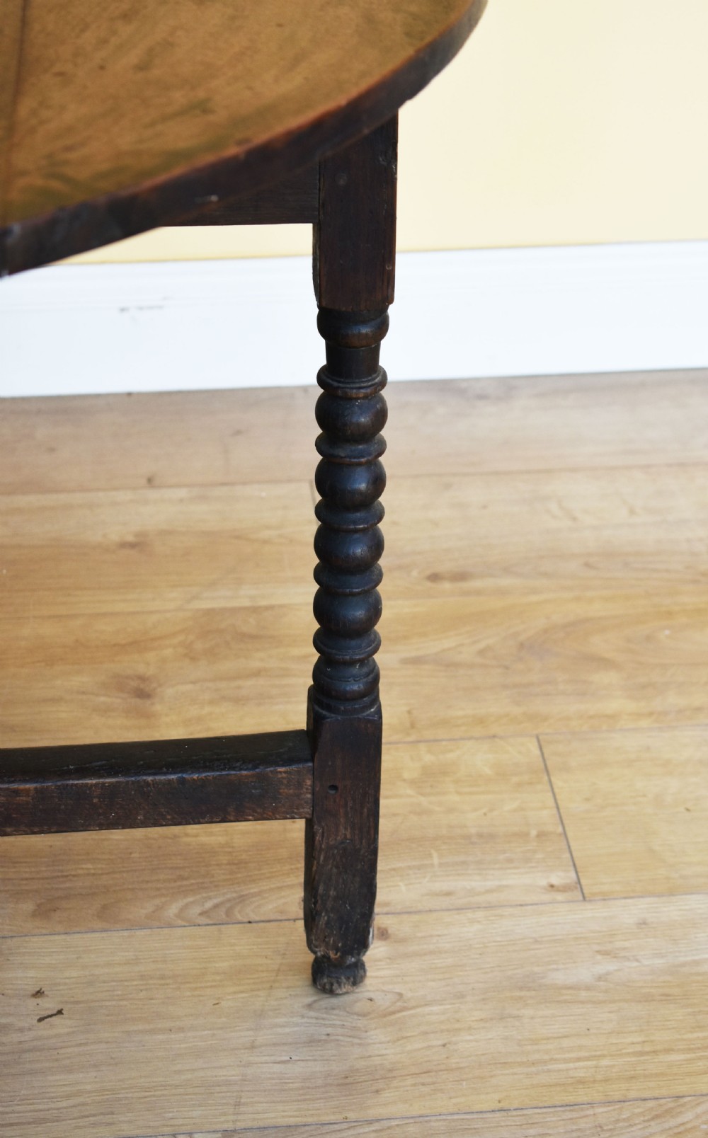An eighteenth-century dark oak gateleg dining table with circular drop leaves and bobbin-turned legs standing on a wooden floor. View III