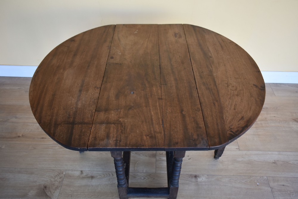 An eighteenth-century dark oak gateleg dining table with circular drop leaves and bobbin-turned legs standing on a wooden floor. View IV