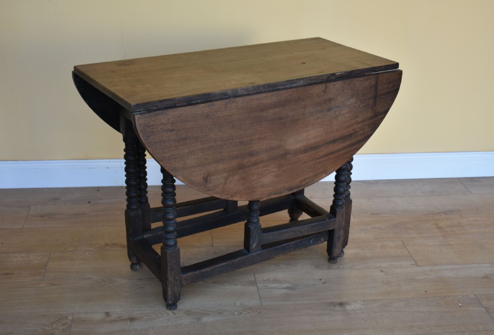 An eighteenth-century dark oak gateleg dining table with circular drop leaves and bobbin-turned legs standing on a wooden floor. View V