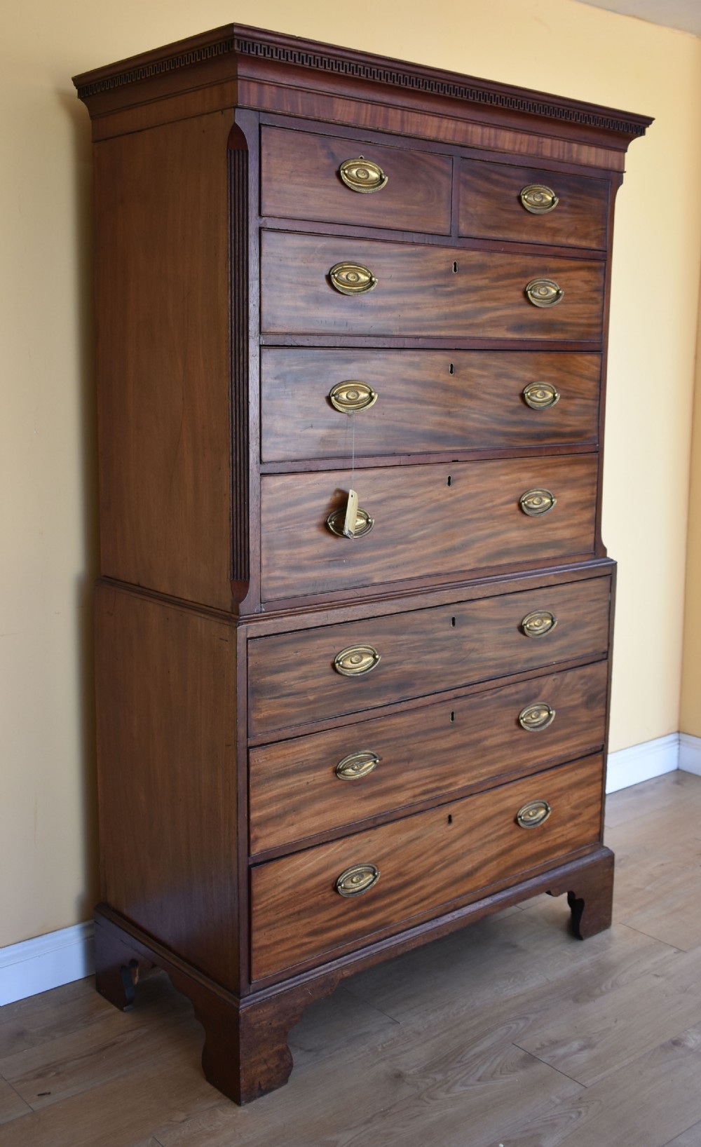A George III mahogany chest-on-chest featuring a dentil-moulded cornice, fluted chamfered corners, brass oval handles, and bracket feet.