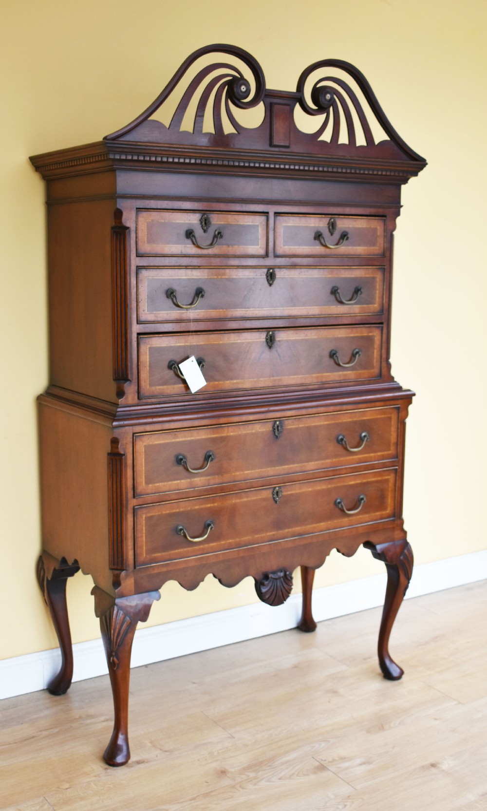 A Georgian style mahogany chest on stand featuring an openwork scrolled pediment, five crossbanded drawers with brass swan-neck handles, and cabriole legs ending in pad feet.