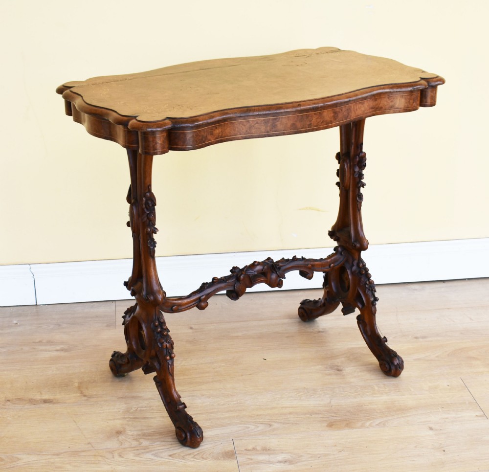 A Victorian burr walnut occasional table featuring a serpentine top with wood inlay, supported by carved legs and a central stretcher.